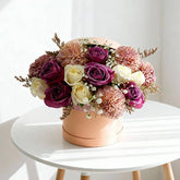 Elegant bouquet of purple and cream roses with pink chrysanthemums in a peach round box on white table