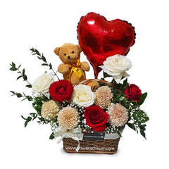 Flower bouquet arrangement with red and white roses, beige flowers, small teddy bear with yellow bow, and red heart balloon in woven basket