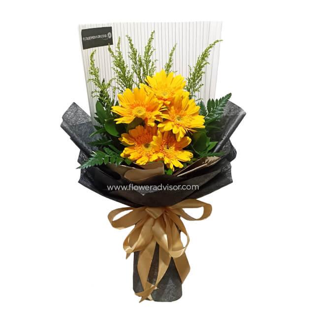 Bright yellow gerbera daisy bouquet with green foliage wrapped in black paper and tied with a gold ribbon