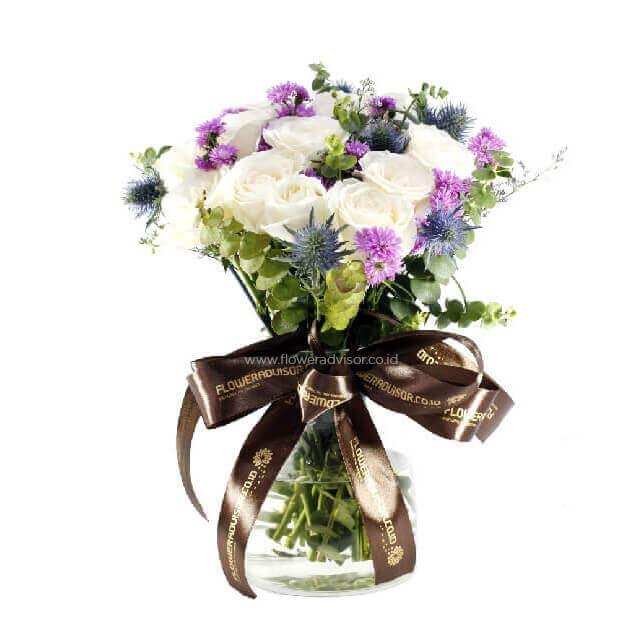 Elegant bouquet of white roses and purple flowers in a clear glass vase with brown FLOWERADVISOR ribbon