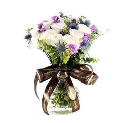 Elegant bouquet of white roses and purple flowers in a clear glass vase with brown FLOWERADVISOR ribbon