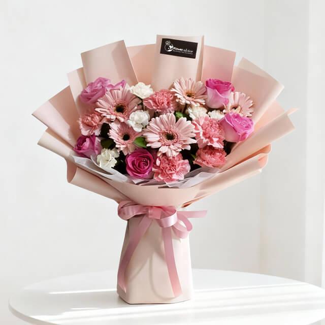 Elegant bouquet of pink roses, carnations, and gerberas wrapped in soft pink paper with ribbon