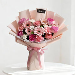 Elegant bouquet of pink roses, carnations, and gerberas wrapped in soft pink paper with ribbon