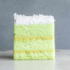 Slice of green pandan cake with coconut cream topping on gray background