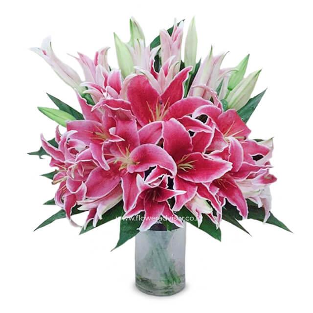 Bouquet of vibrant pink lilies with lush green leaves in a clear glass vase, fresh flower delivery