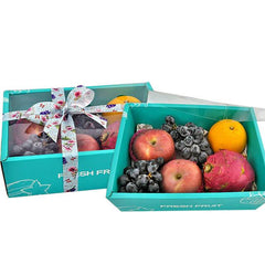 Fresh fruit gift box with apples, grapes, orange, and dragon fruit in teal packaging with floral ribbon