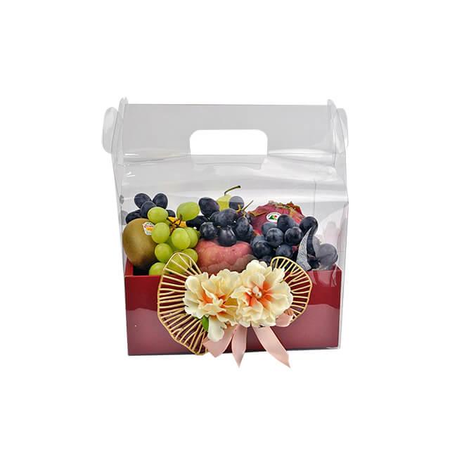 Fruit gift box with green and black grapes, kiwi, apples, decorated with flowers and pink ribbon