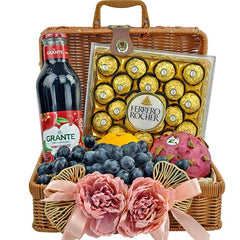 Wicker gift basket with Ferrero Rocher chocolates, pomegranate juice, grapes, dragon fruit, orange, and pink flower decorations
