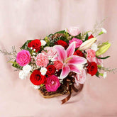 Elegant flower basket with pink lilies, red and pink roses, carnations, and white filler flowers on light pink background