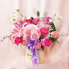 Elegant bouquet with pink roses, lilies, carnations, and purple accents in a cream vase with purple ribbon