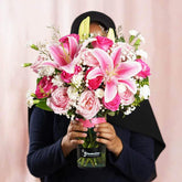 Person holding a vibrant bouquet of pink lilies, roses, and white flowers in a clear FlowerAdvisor vase