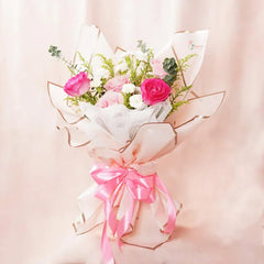 Pink and white rose bouquet with greenery wrapped in white paper and tied with pink ribbon