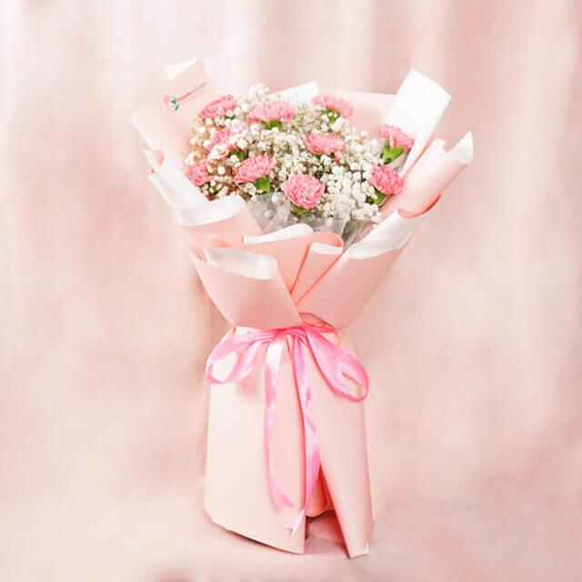 Pink carnation bouquet with white baby's breath flowers wrapped in soft pink paper and tied with a pink ribbon
