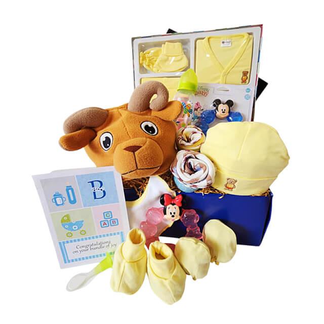 Baby gift hamper with yellow clothes, stuffed ram toy, Minnie Mouse teether, baby bottle, and accessories