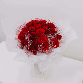 Bouquet of fresh red roses with pink baby's breath in white wrapping on white background