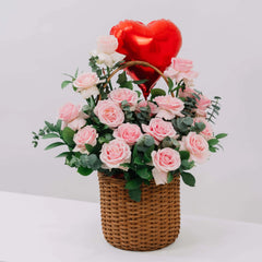 Wicker basket bouquet with fresh pink roses, green leaves, and a red heart-shaped balloon for flower delivery