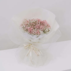 Delicate pink and white baby's breath flower bouquet wrapped in white paper and mesh with ribbon
