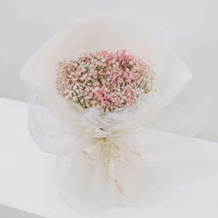 Delicate bouquet of pink and white baby’s breath flowers wrapped in white translucent paper with branded ribbon