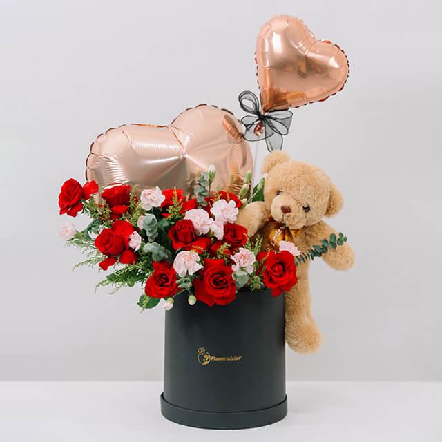 Elegant black vase with fresh red and pink roses, a teddy bear, and two rose gold heart-shaped balloons