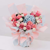 Fresh flower bouquet with pink roses, blue hydrangea, and white pompom flowers in pastel wrap