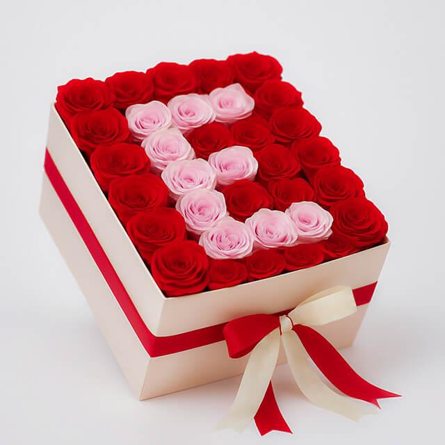Box of red and pink roses arranged in flower bouquet with letter E design, tied with red and cream ribbon