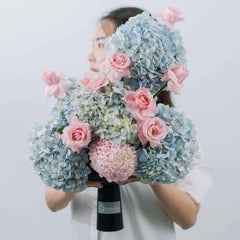 Woman holding a fresh bouquet of blue hydrangeas and pink roses in a black vase with FlowerAdvisor label