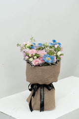 Pink and blue mixed flower bouquet wrapped in burlap with black FlowerAdvisor ribbon on white surface
