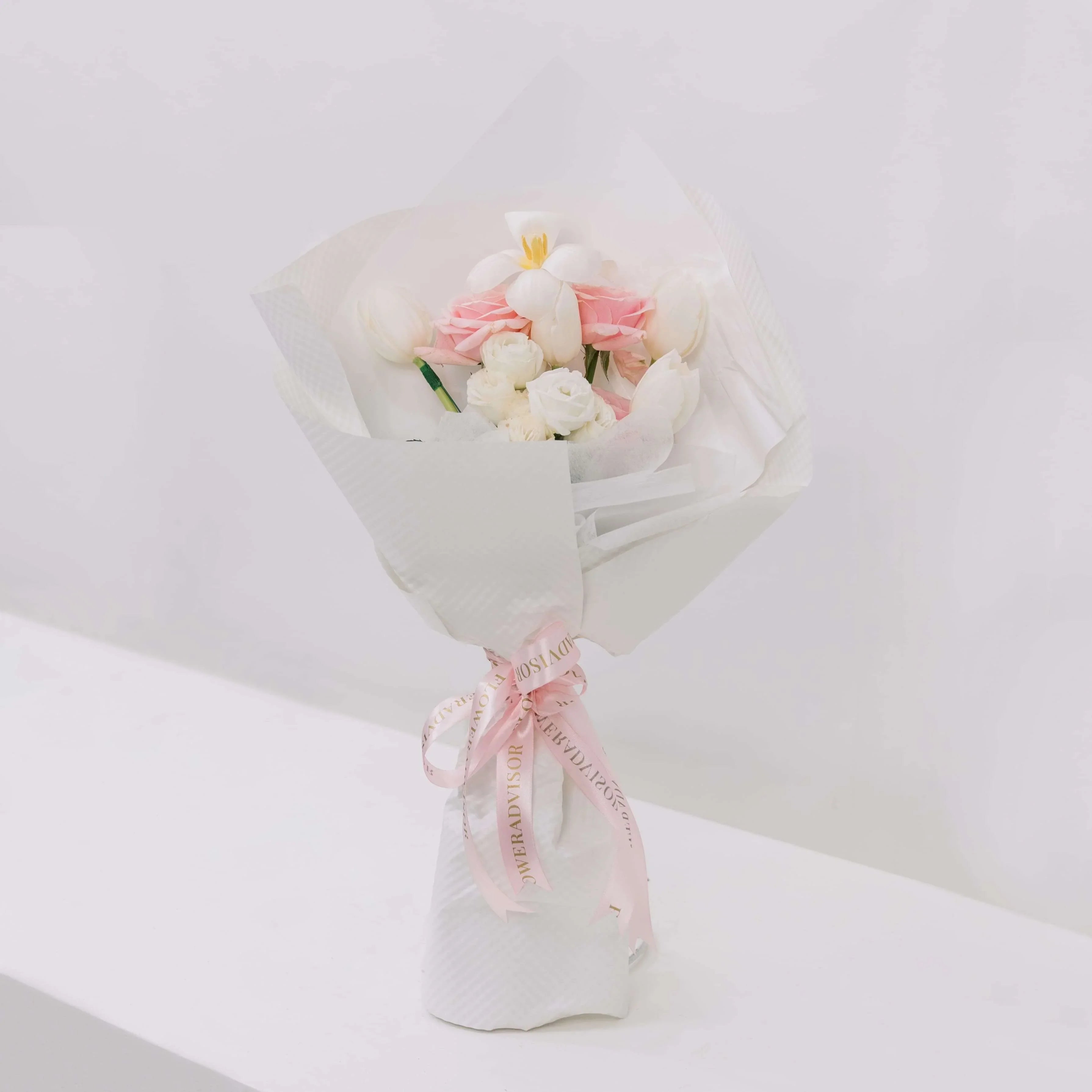 Elegant bouquet with white tulips, pink roses, and white flowers wrapped in white paper with pink FlowerAdvisor ribbon
