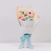 Elegant bouquet with pink gerbera, carnations, white flowers wrapped in white paper tied with blue ribbon