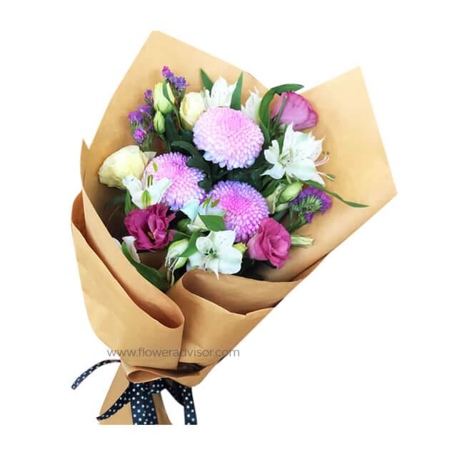 Bouquet of pink chrysanthemums, white lilies, and purple flowers wrapped in brown paper with black polka dot ribbon