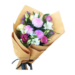 Bouquet of pink chrysanthemums, white lilies, and purple flowers wrapped in brown paper with black polka dot ribbon
