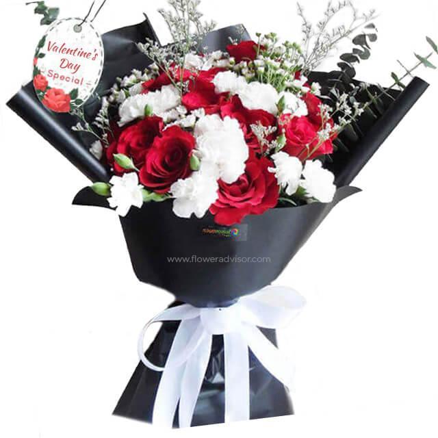 Valentine's Day bouquet with red roses, white carnations, and greenery in black wrap
