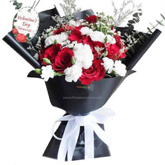 Valentine's Day bouquet with red roses, white carnations, and greenery in black wrap