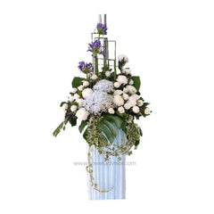 Elegant floral arrangement with white roses, blue hydrangea, purple flowers, and green foliage in tall vase