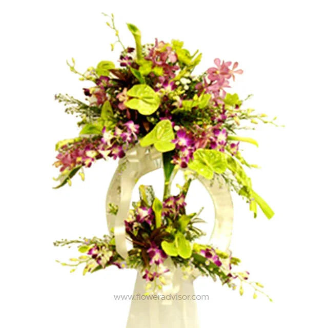 Elegant two-tier floral arrangement with purple orchids and green anthuriums on white stand