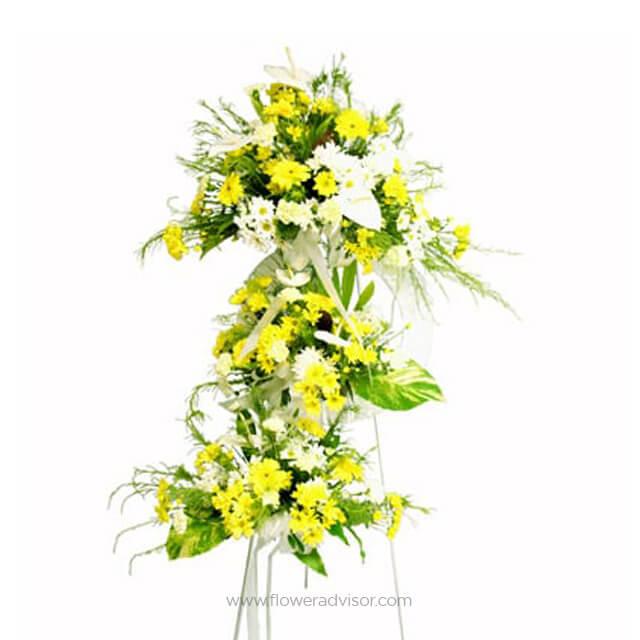 Standing floral arrangement with yellow and white flowers and green leaves on white background