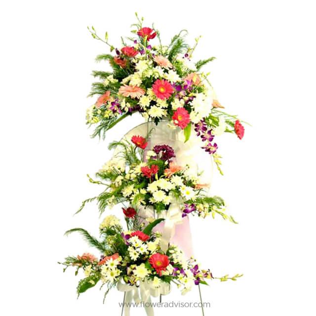 Three-tier colorful flower arrangement with red, pink, white, yellow blooms and green foliage on white background