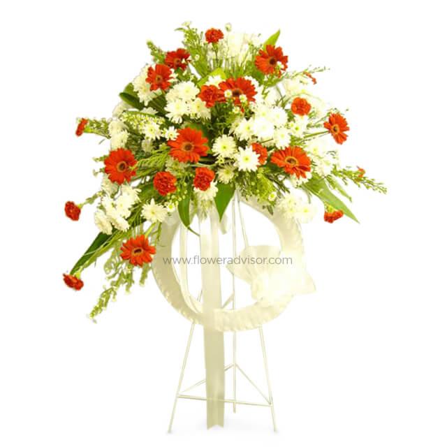 Standing funeral wreath with orange gerbera daisies and white flowers on white stand