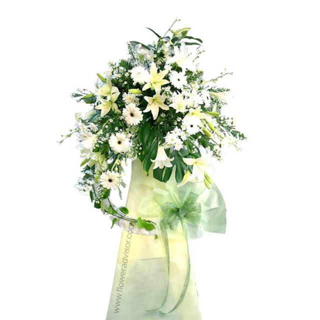 Elegant white and cream flower arrangement with lilies and daisies in a green vase with ribbon