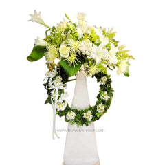 White and green floral funeral wreath arrangement with lush flowers and greenery on white stand