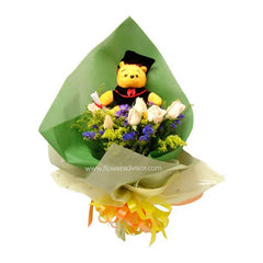 Graduation bouquet with pink roses, purple flowers, and a plush bear in cap and gown wrapped in green paper