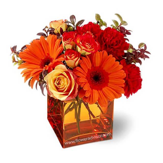 Vibrant floral arrangement with orange gerberas and red roses in a glass vase