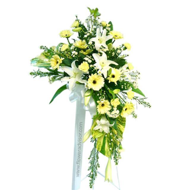 Elegant flower arrangement with white lilies, yellow daisies, greenery, and white ribbon