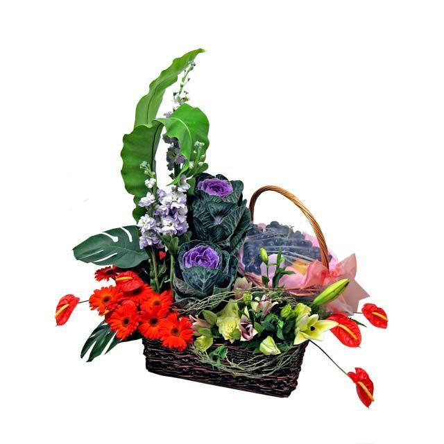 Fruit and flower arrangement in a wicker basket with lilies, gerberas, and greenery