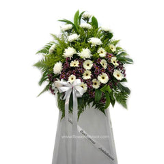 Standing funeral flower arrangement with white chrysanthemums, daisies, greenery, and a white bow