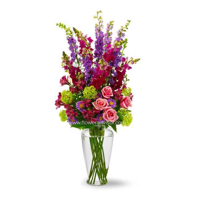 Mixed fresh flowers in a glass vase with roses, snapdragons, and green filler on white background