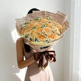 Woman holding large bouquet of peach roses and white baby's breath in soft pastel wrapping