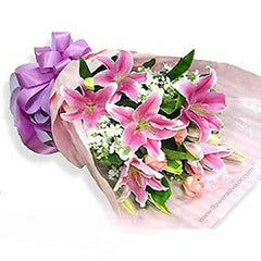 Bouquet of fresh pink lilies with white flowers wrapped in pink paper and a purple ribbon