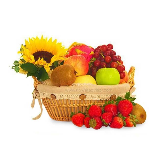 Wicker basket with sunflower, assorted fresh fruits including grapes, kiwi, apple, dragon fruit, and strawberries