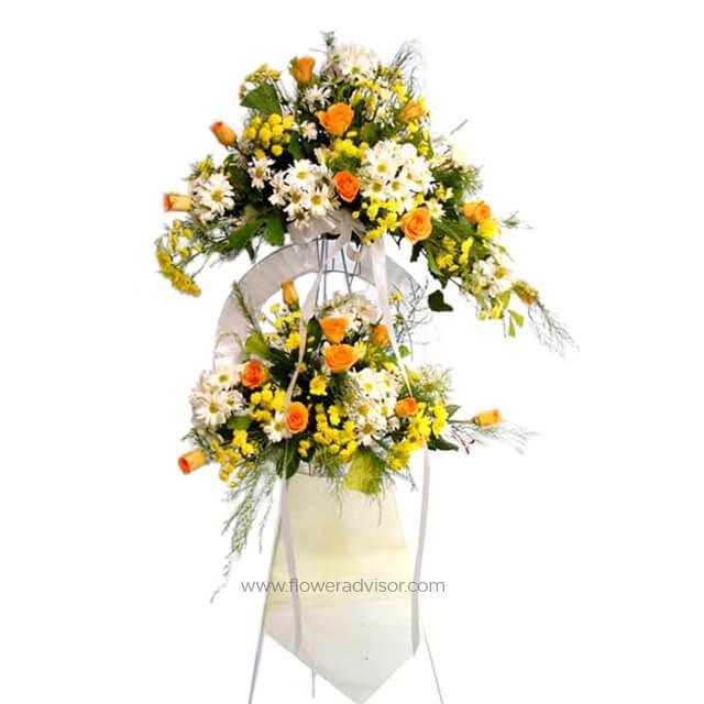 Standing flower arrangement with orange roses, white daisies, and yellow blooms on a stand